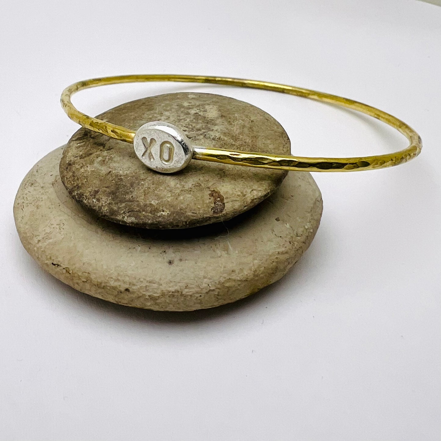 Brass bracelet with a silver charm on a stack of stones