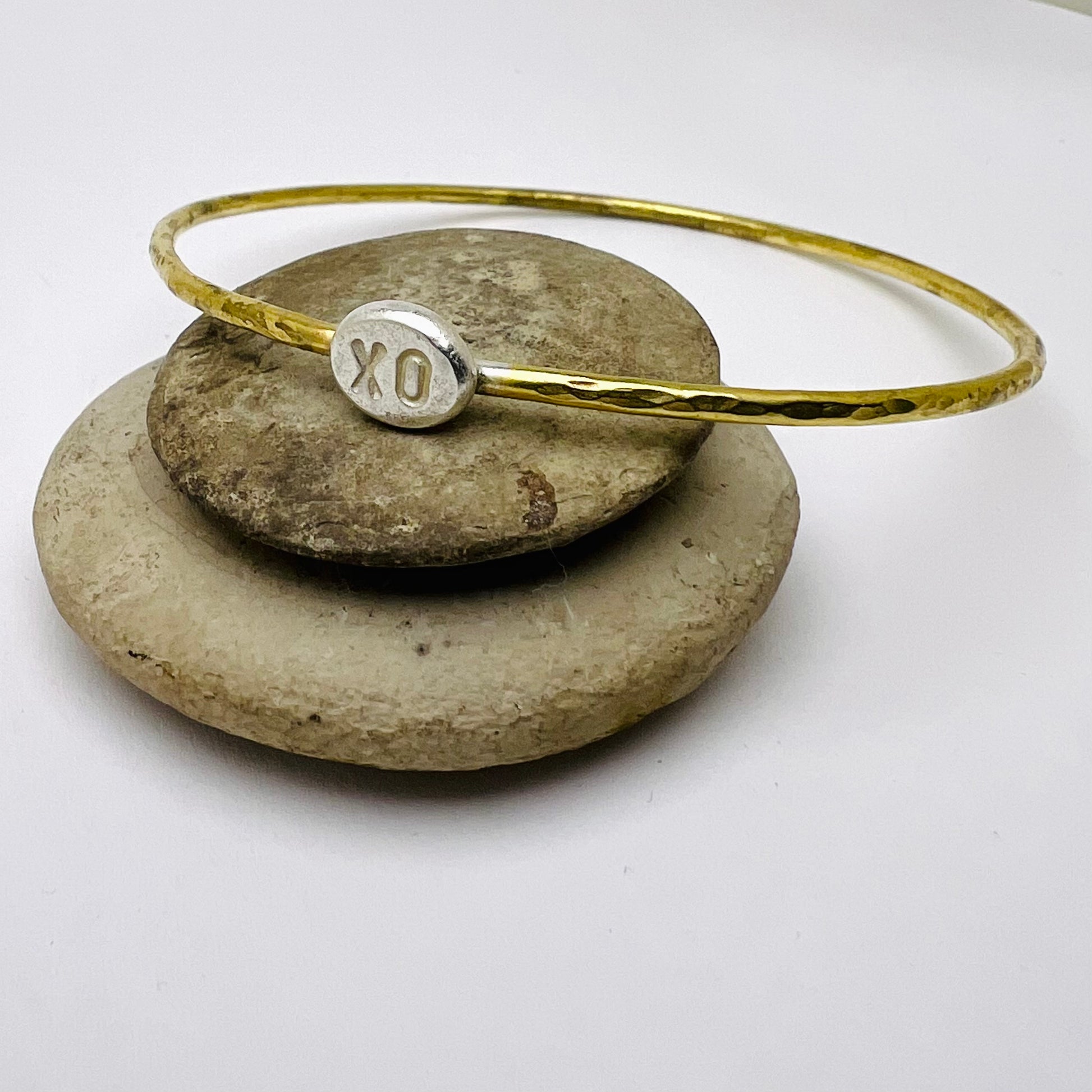 Brass bracelet with a silver charm on a stack of stones
