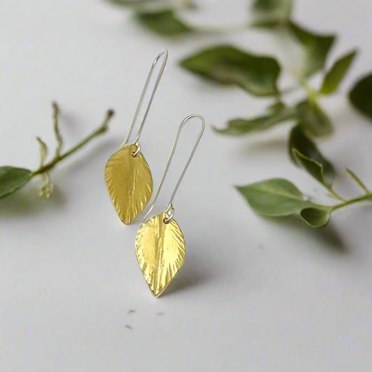 Silver and brass earrings with brass leaves dangling from silver ear wire