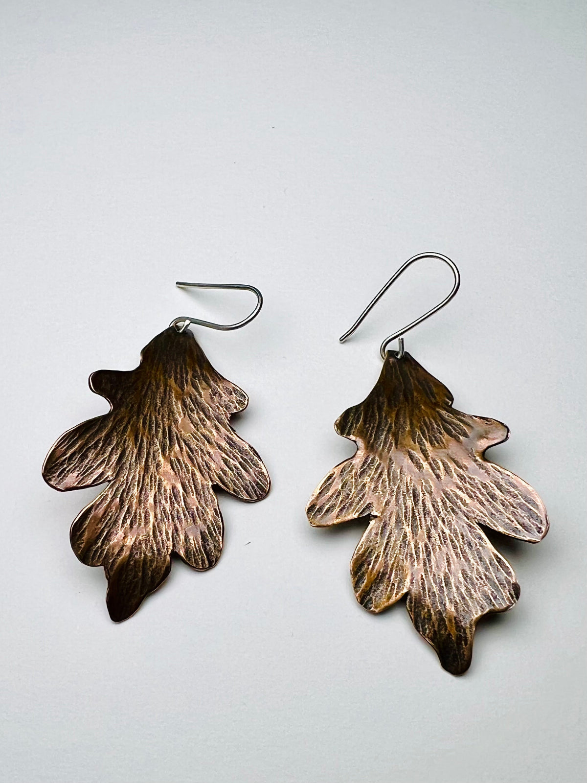 Pair of oak leaf-shaped earrings on a light gray background