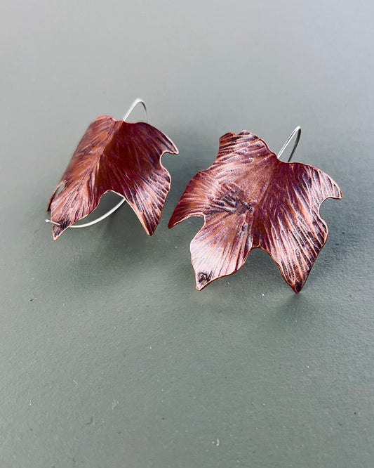 Pair of copper leaf-shaped earrings on a gray background