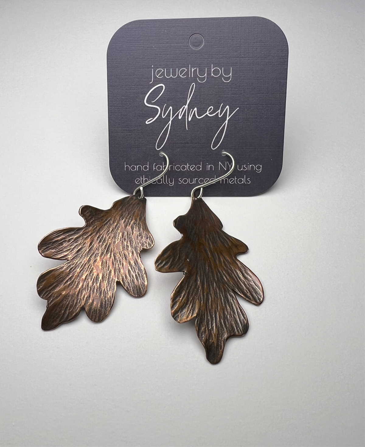 Copper leaf-shaped earrings on a card against a light gray background