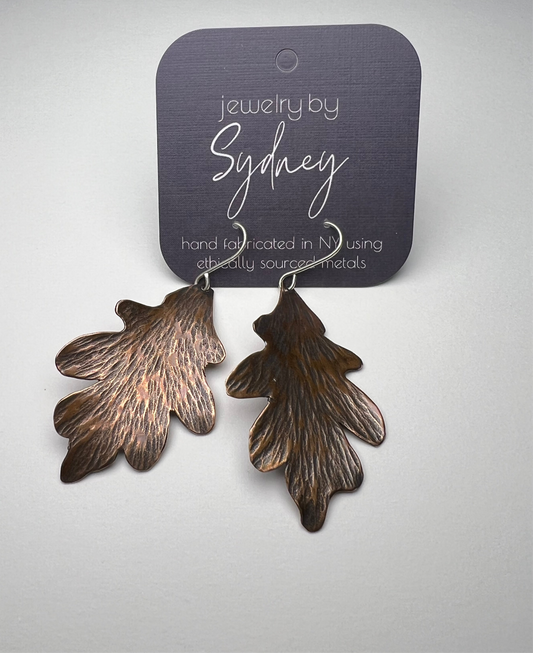 Copper leaf-shaped earrings on a card against a light gray background