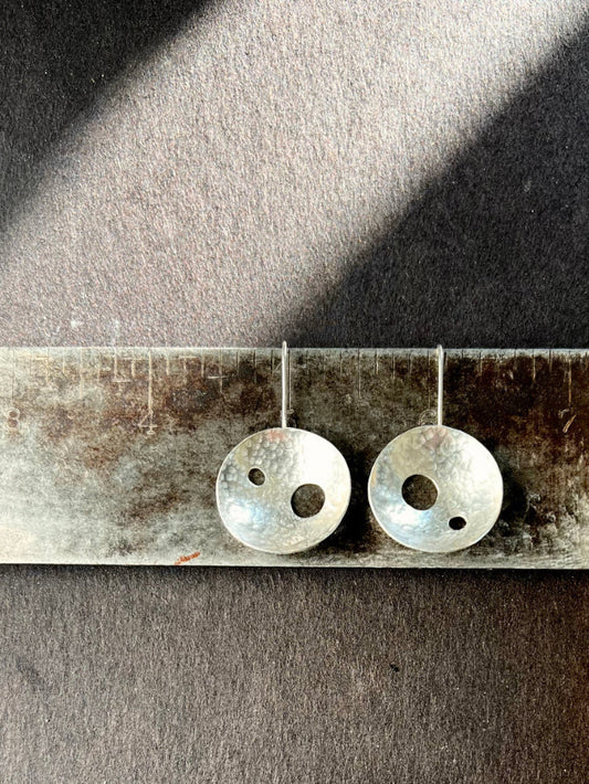 Pair of silver dome earrings with cutout holes on an antique square against a dark background