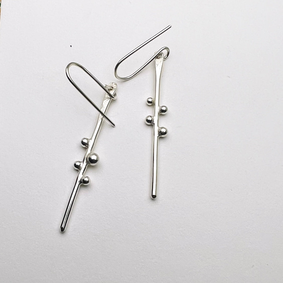 Silver branch-like earrings with small spherical silver balls on a white background