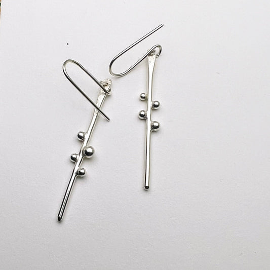 Silver branch-like earrings with small spherical silver balls on a white background