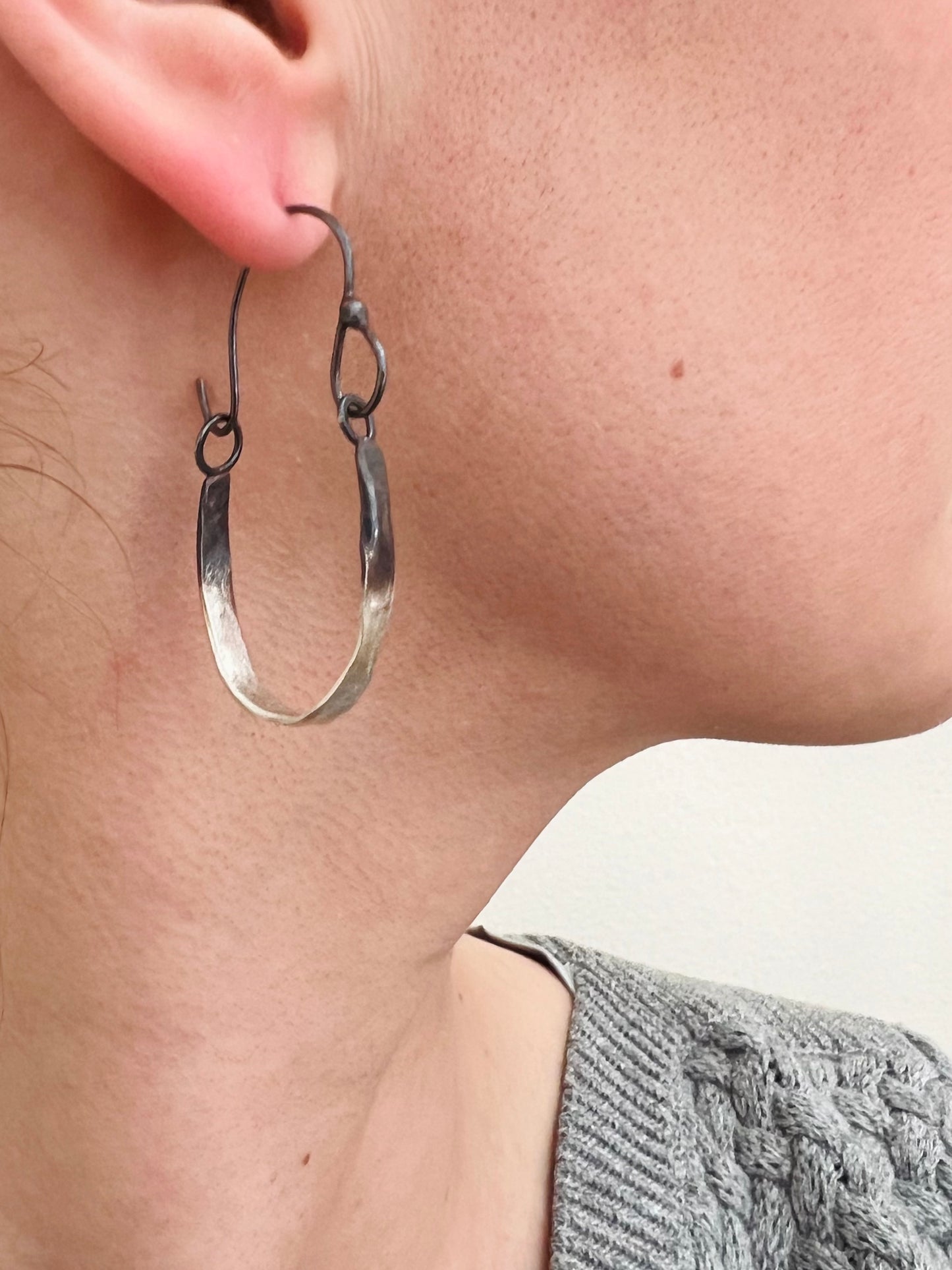 Handmade Silver hoop earring worn by a person with a neutral background.