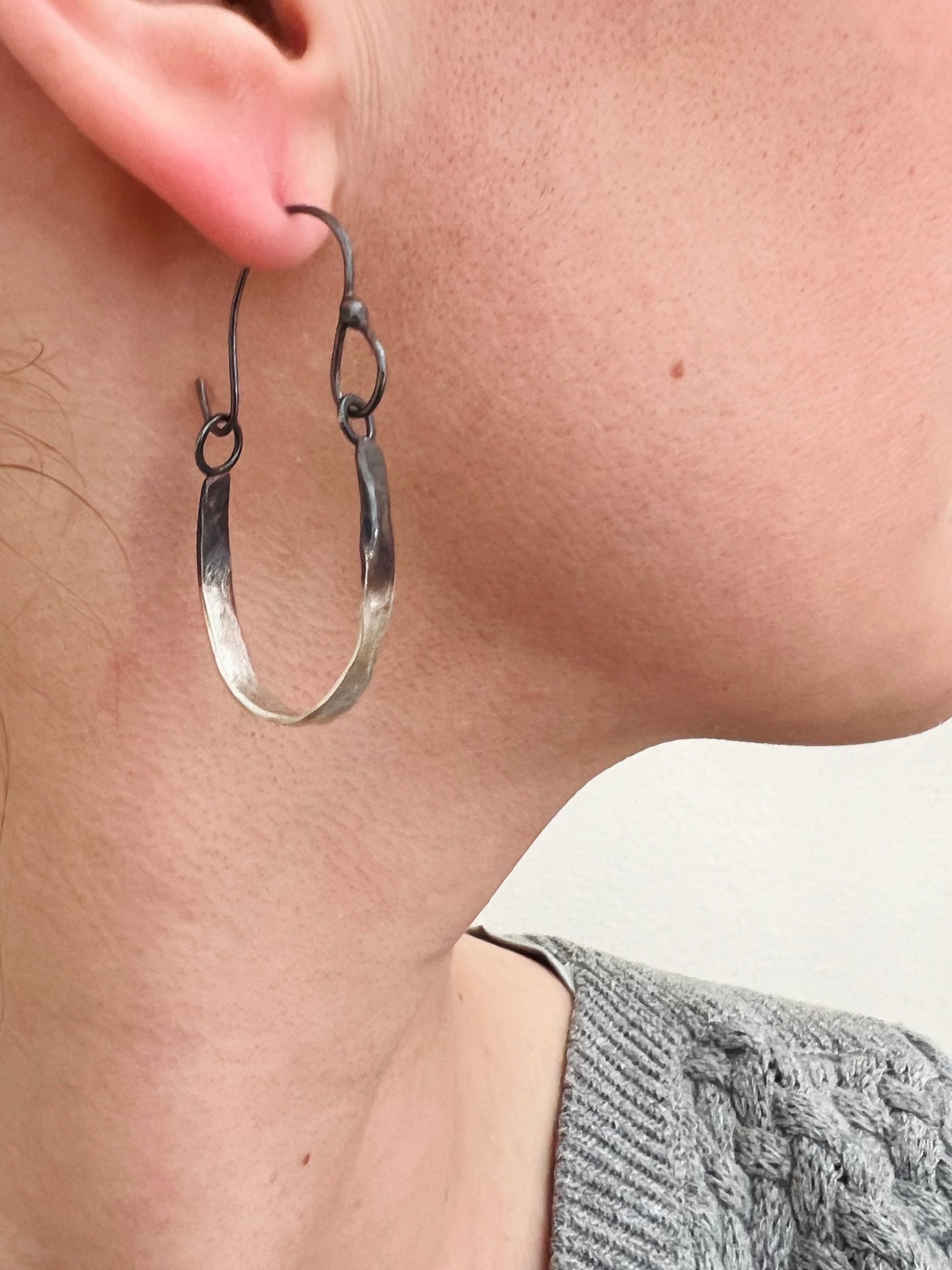 Handmade Silver hoop earring worn by a person with a neutral background.