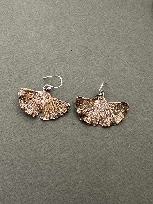 Copper ginkgo leaf-shaped earrings on a gray background.