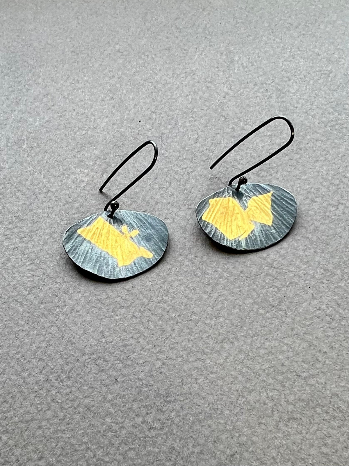 Pair of  fan shaped earrings with gold and oxidized silver on a gray background
