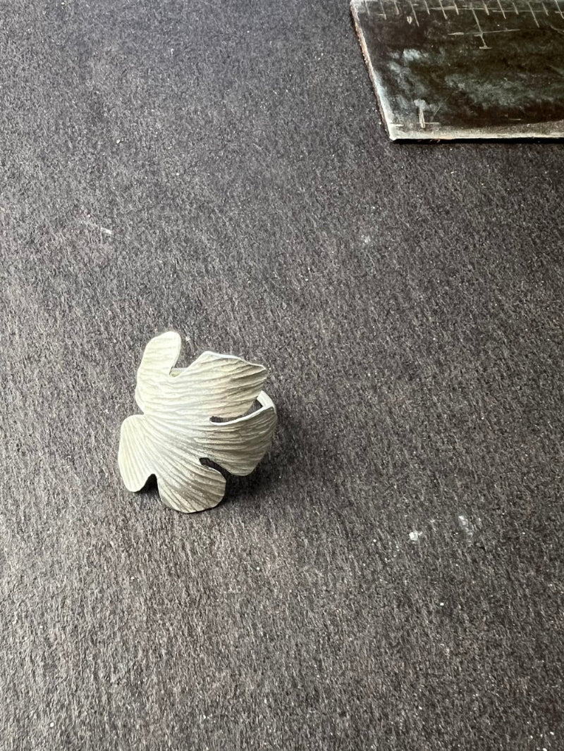 Silver leaf-shaped object on a gray surface with a ruler in the background