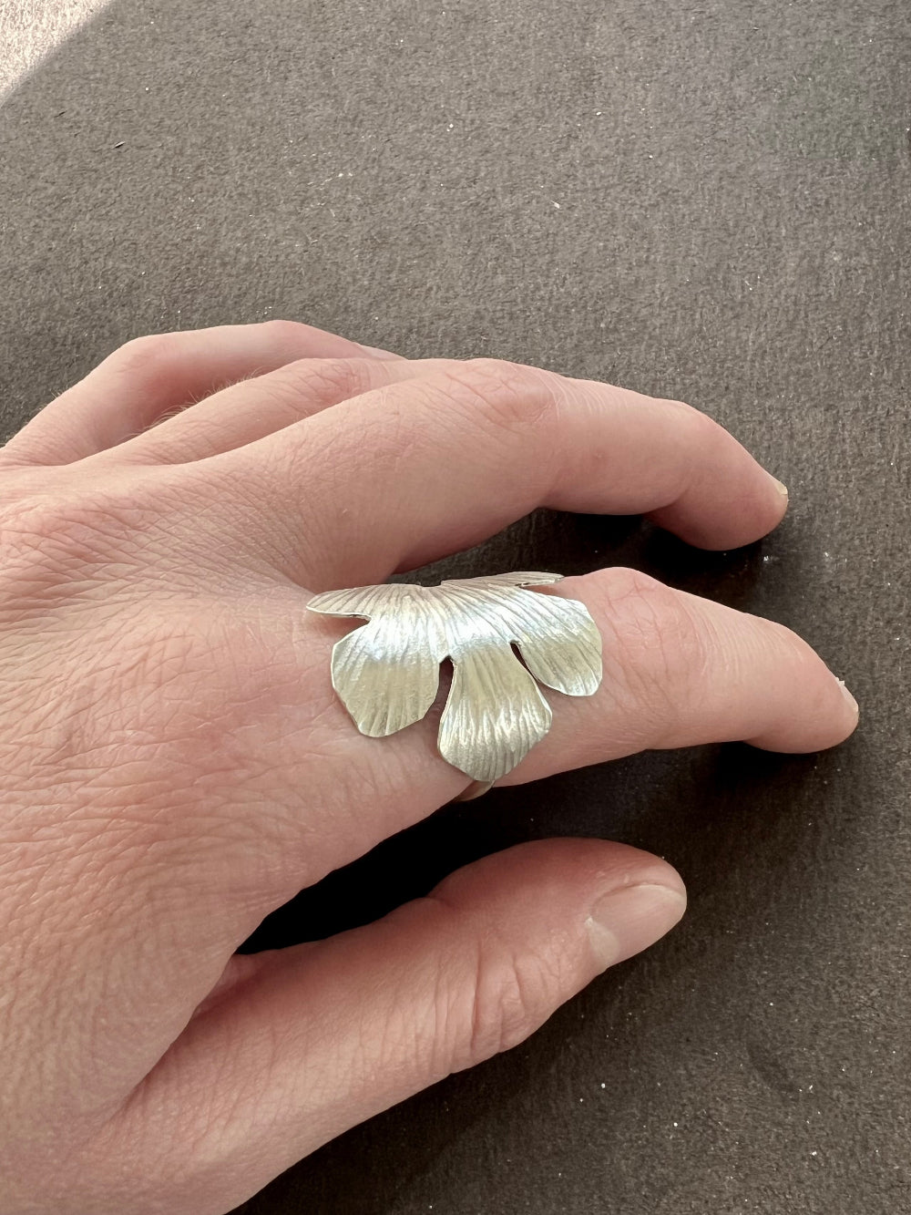 Hand wearing a silver fig leaf ring on a brown surface