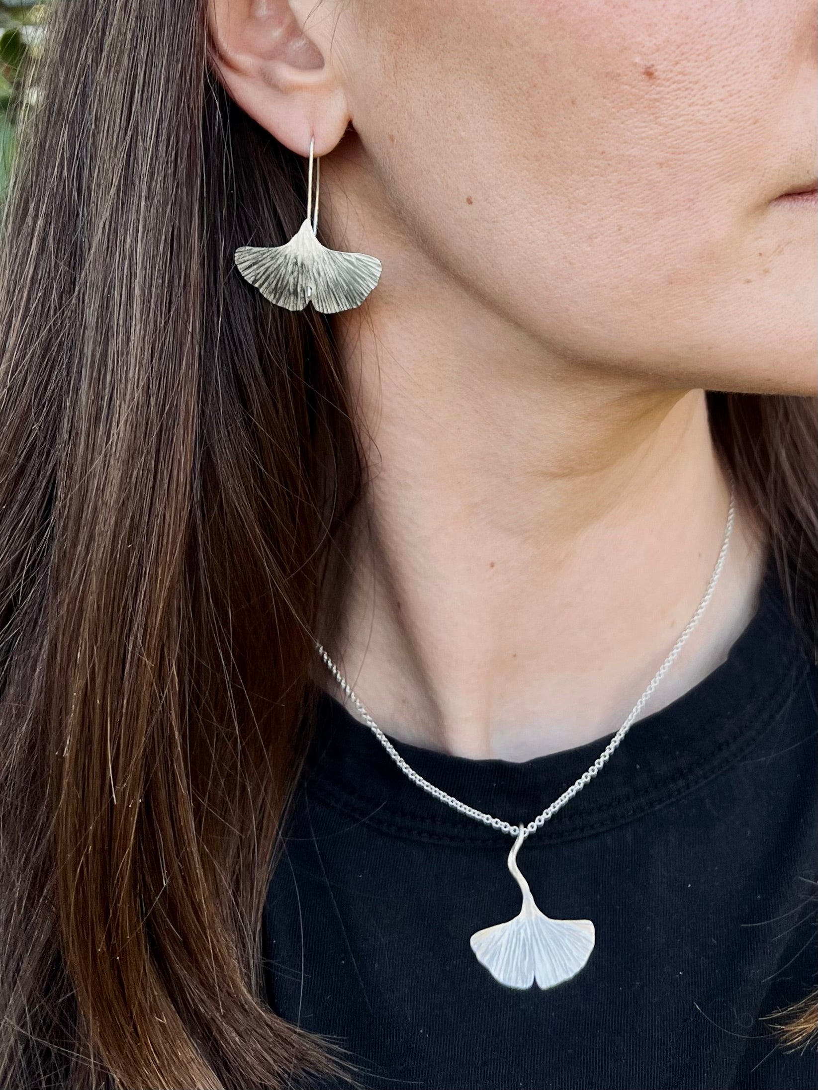 Close-up of a person wearing silver ginkgo leaf earrings and necklace.