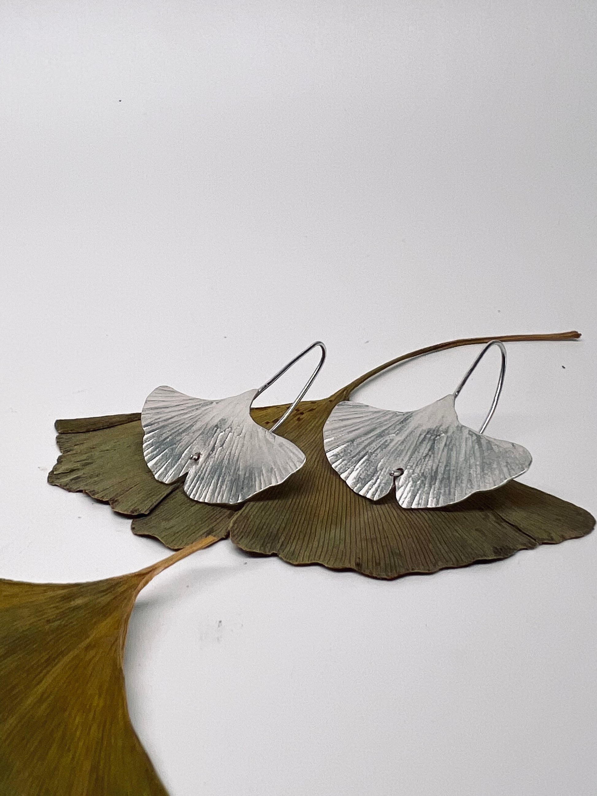 Silver leaf-shaped earrings on a white background with ginkgo leaves.