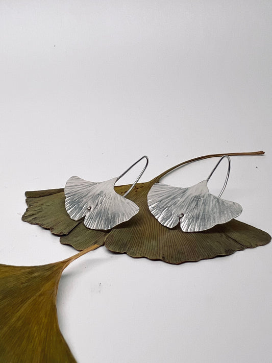 Silver leaf-shaped earrings on a white background with ginkgo leaves.