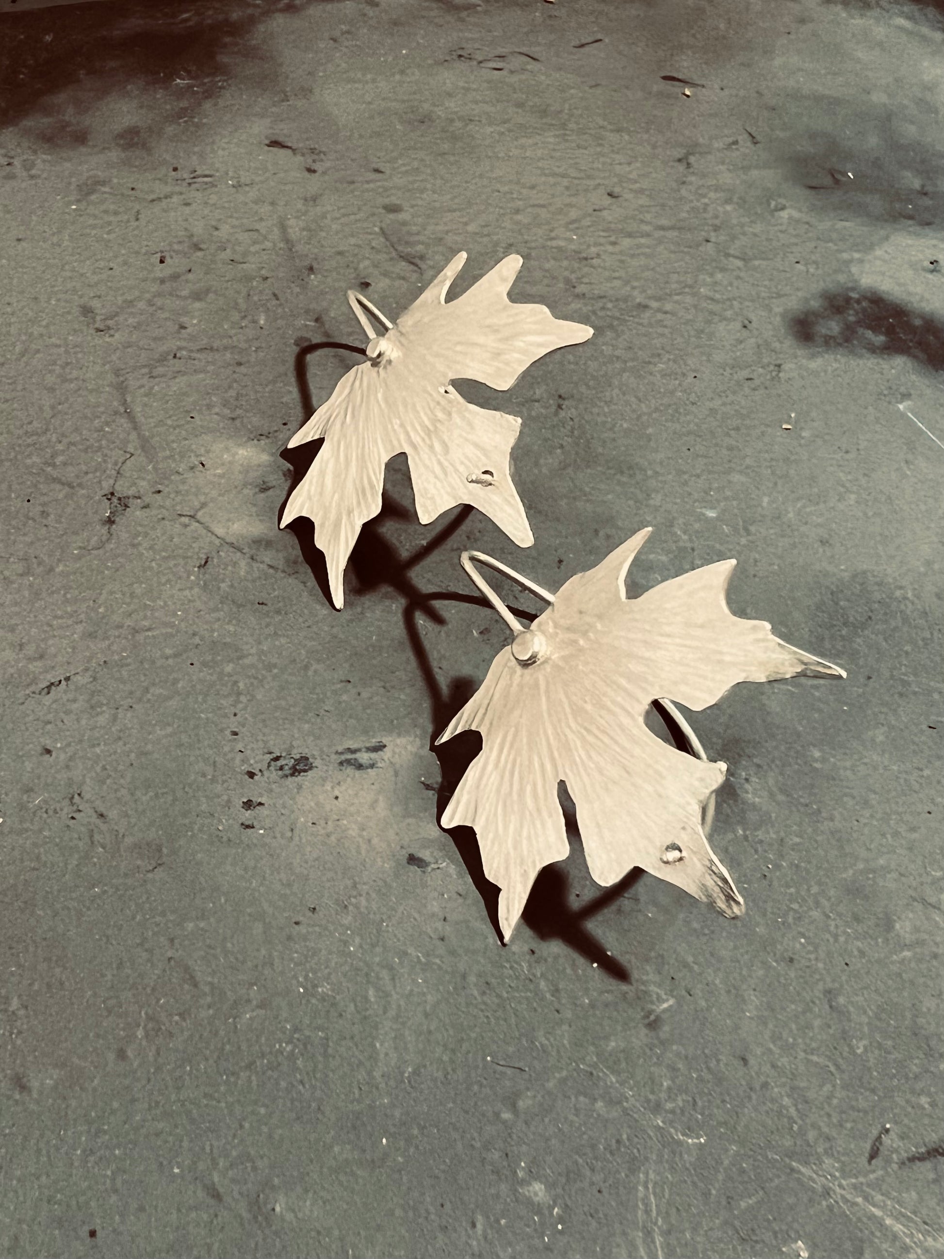 Pair of silver leaf-shaped earrings on a textured surface