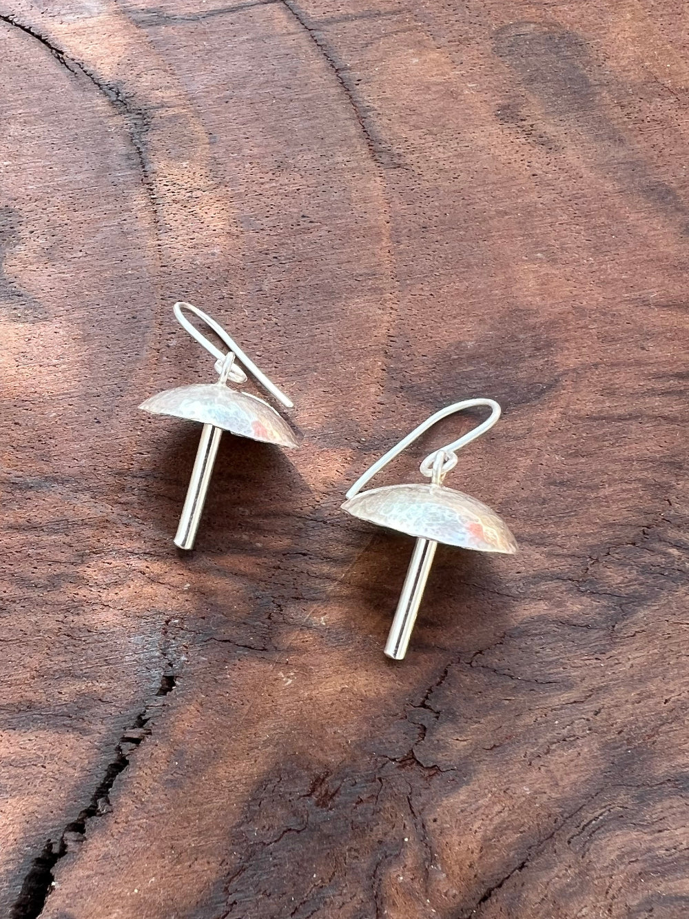 Pair of silver mushroom earrings on a wooden surface