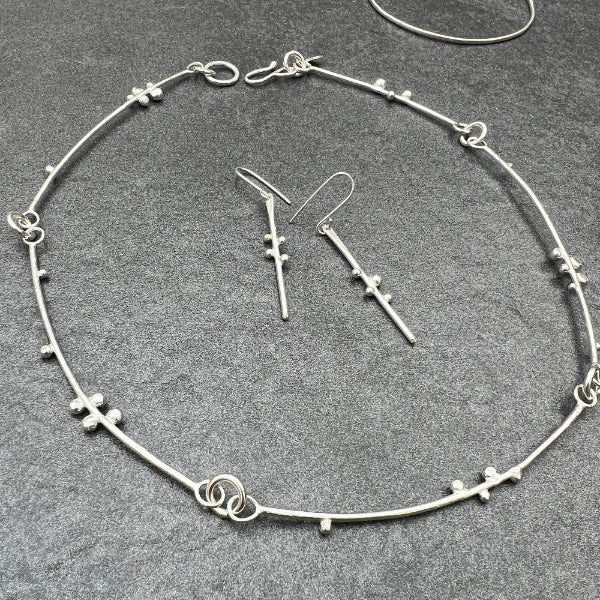 Silver handmade necklace made from bars of silver with decorative silver balls attached to resemble budding branches.