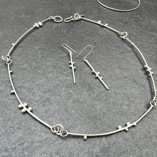 Silver handmade necklace made from bars of silver with decorative silver balls attached to resemble budding branches.