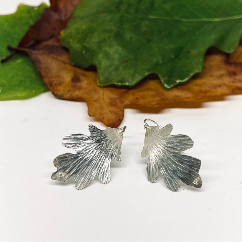 Silver leaf-shaped earrings on a white background with green and brown leaves.