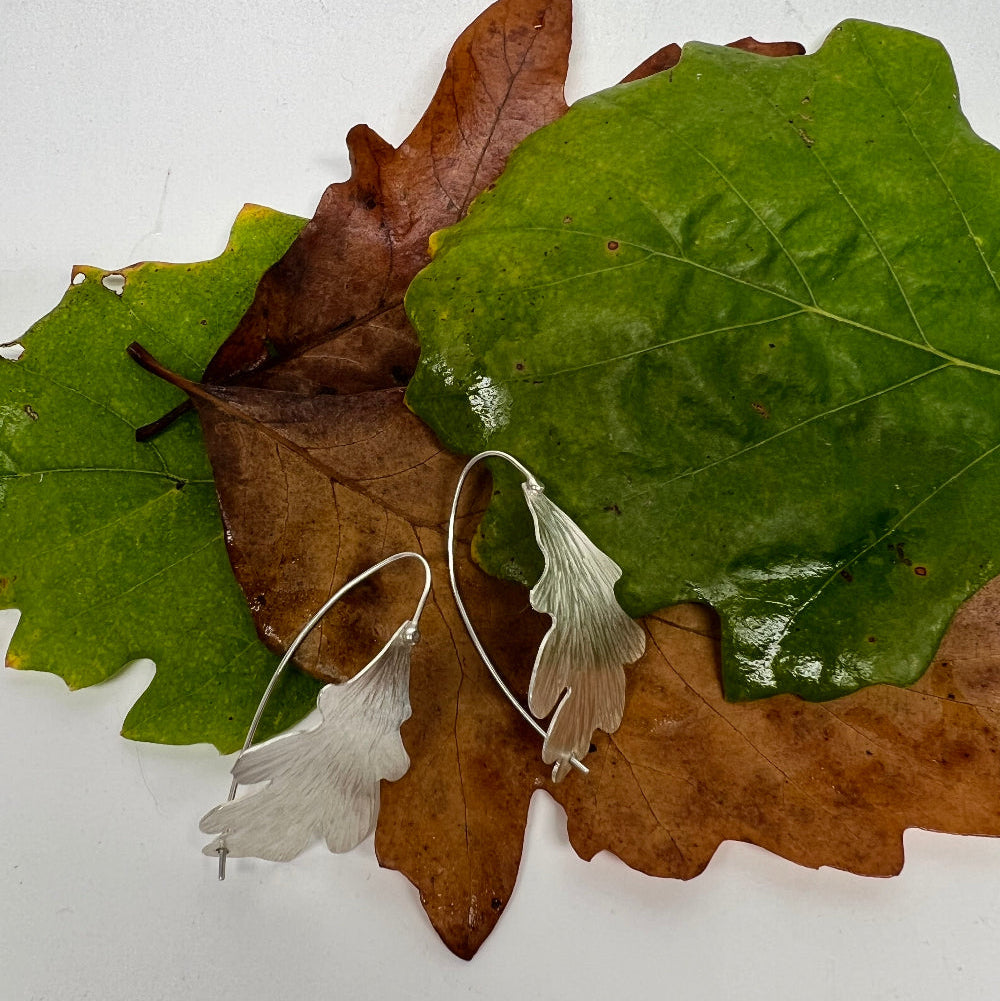 Silver oak earrings on a leafy background