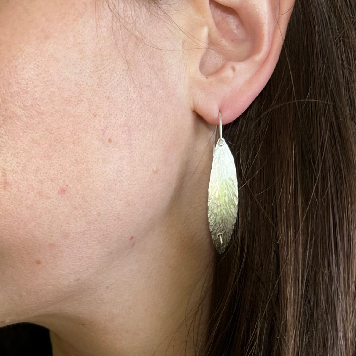 Close-up of a person wearing a silver earring with a textured design.