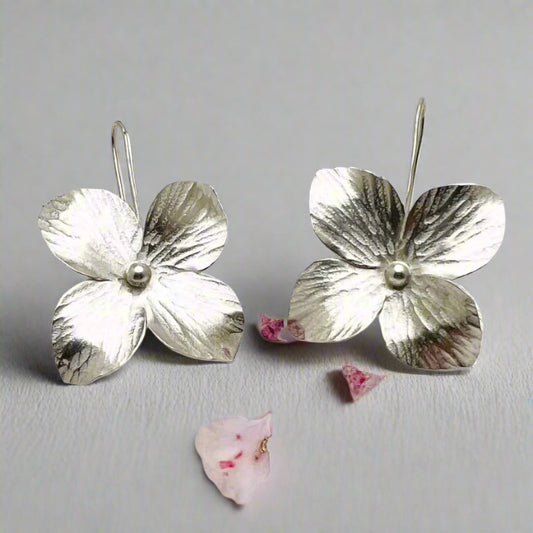 Silver flower-shaped earrings on a gray background with pink petals.