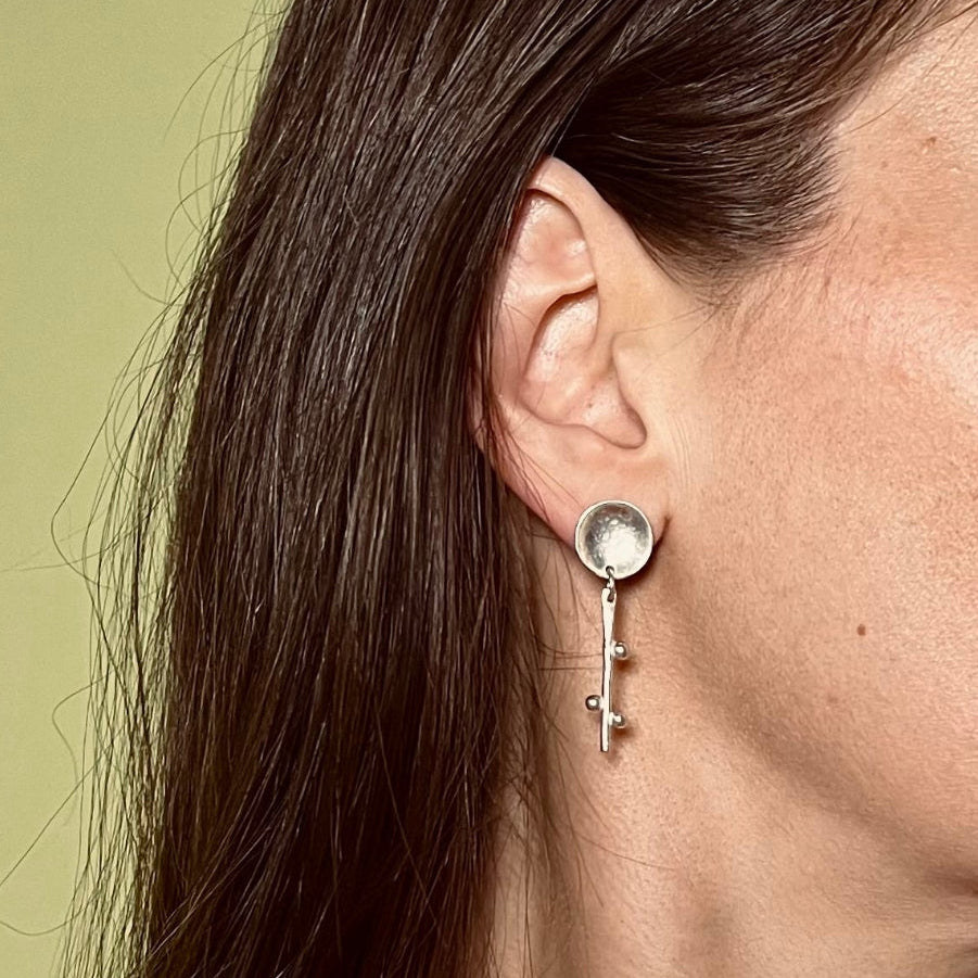 Close-up of a woman wearing a silver earring with a green background