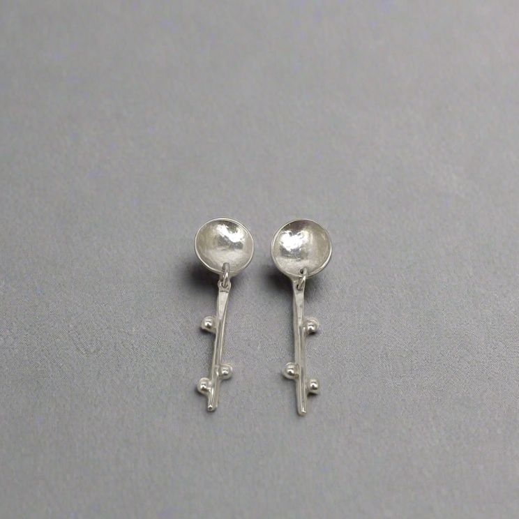 Silver spoon-shaped earrings on a gray background
