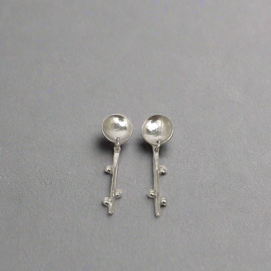 Silver spoon-shaped earrings on a gray background