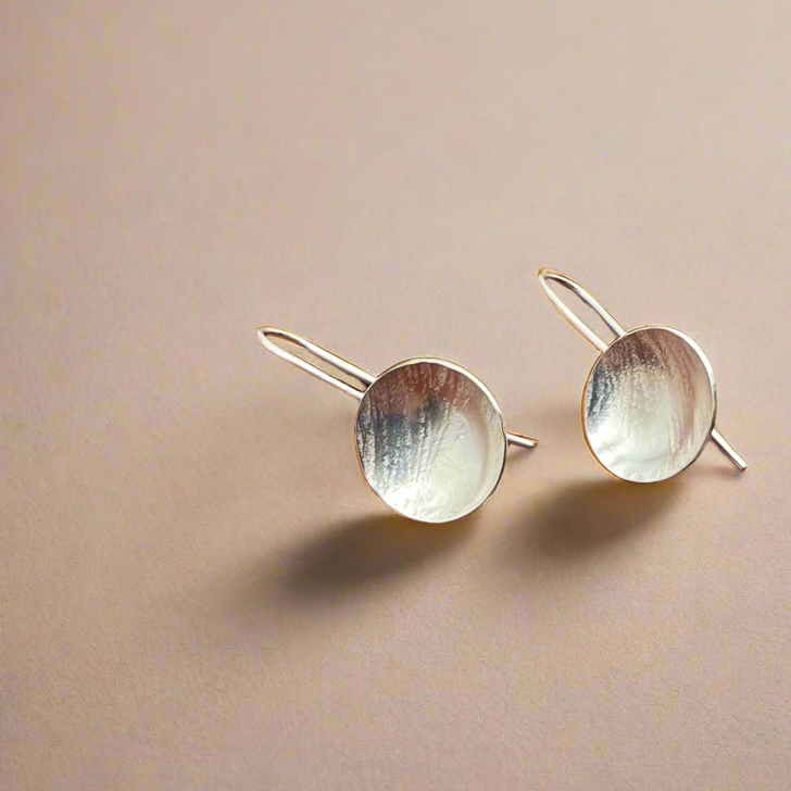 Pair of silver earrings with round tops on a beige background.