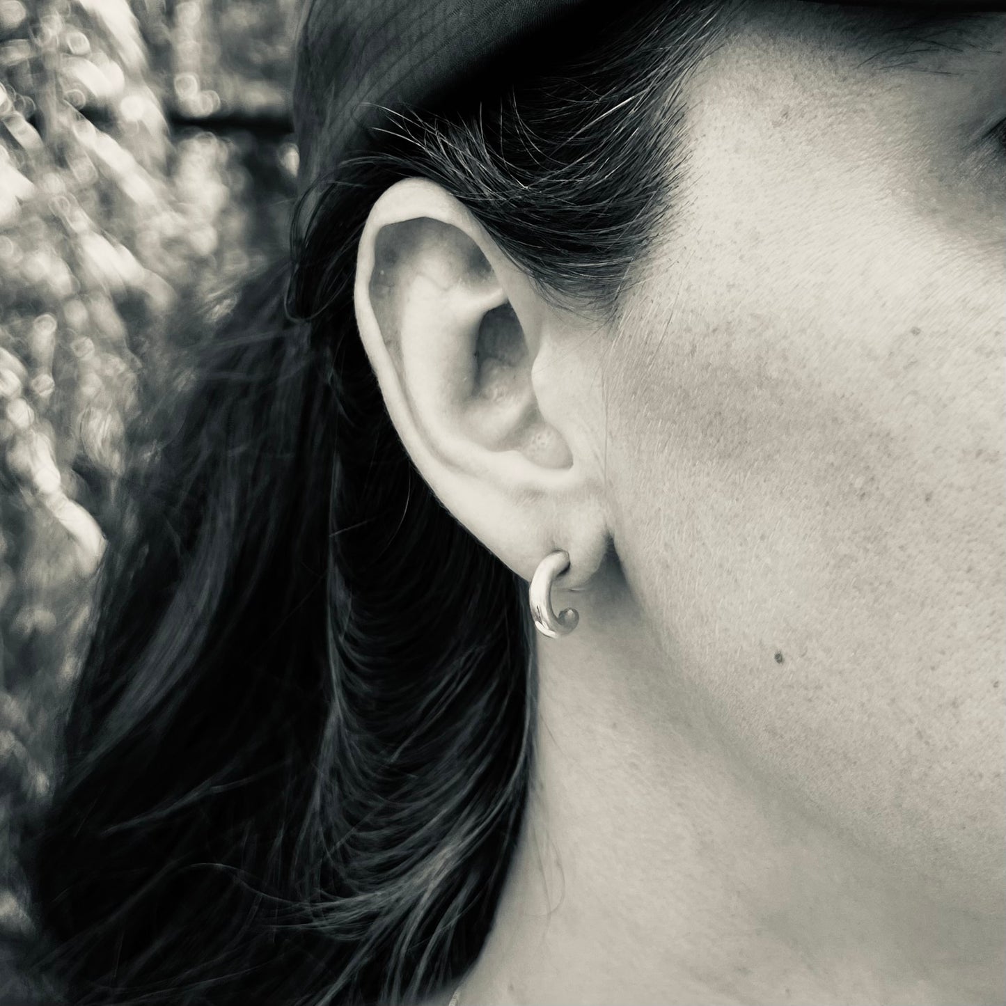 Close-up of ear with a small silver thick hoop earring, hair partially covering the face.